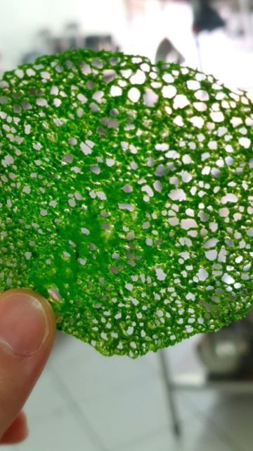 Bright green, porous mesh scrubber held between a thumb and finger.