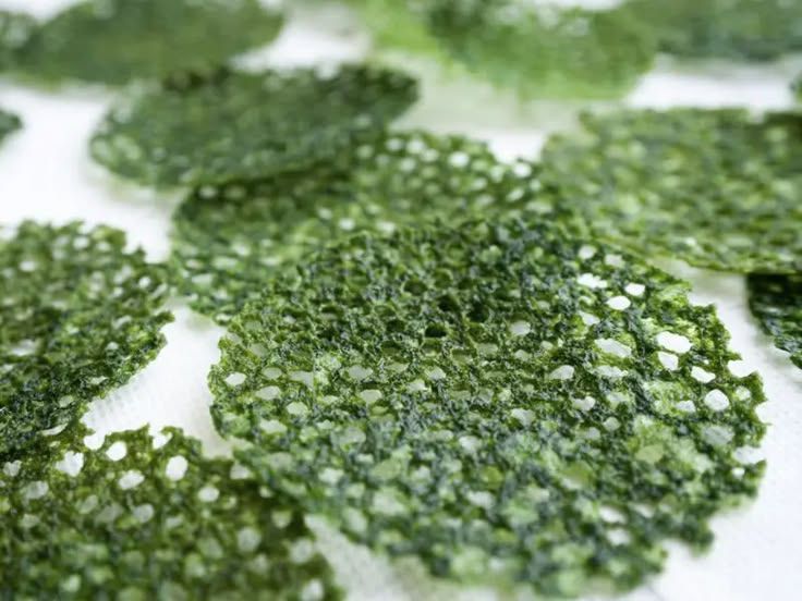 Close-up of crispy green kale chips spread on a white surface.